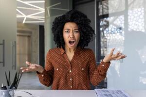 afrikanisch amerikanisch Geschäftsfrau sieht aus frustriert und spricht animiert während ein Treffen von ihr modern Büro. Konzept von Arbeit Stress und Kommunikation. foto