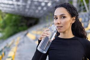 ein jung aktiv Frau nimmt ein Wasser brechen draußen nach trainieren, verkörpern ein gesund Lebensstil und Fitness. foto