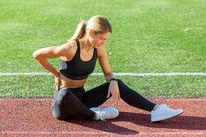 gewidmet jung Frau im Sportbekleidung Dehnen ihr Bein Muskeln auf ein sonnig Spur Feld, verkörpern ein gesund Lebensstil. foto