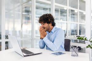 glücklich froh spanisch Geschäftsmann Innerhalb Büro lesen online glücklich Nachrichten auf Laptop, jung Unternehmer feiern erfolgreich Leistung Ergebnisse. foto