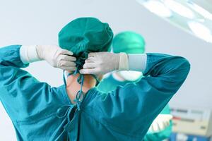 Rückansicht des Chirurgen, der in Vorbereitung eine chirurgische Kappe bindet, medizinisches Team, das chirurgische Eingriffe im Operationssaal durchführt, Teamchirurg bei der Arbeit im Operationssaal foto