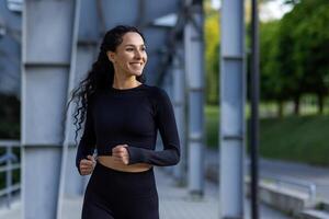 jung schön spanisch Frau mit lockig Haar Joggen in der Nähe von Stadion, Frau im Trainingsanzug lächelnd zufrieden, Laufen im Park. foto