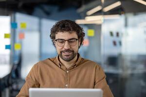 Fachmann männlich Unternehmer mit Brille mit Computer im ein zeitgenössisch Büro Einstellung, reflektieren Produktivität und Fokus. foto