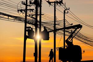 Die Silhouette des Elektrikers klettert auf einen Mast und verwendet eine Seilbahn, um ein Hochspannungsleitungssystem zu warten, Schatten des Elektrikers, Lineman, Reparaturarbeiter bei Kletterarbeiten am Strommast foto