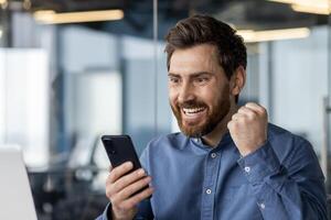 heiter männlich Fachmann im Büro Jubel gut Nachrichten auf Telefon. aufgeregt, erfolgreich und Technologie Konzepte im korporativ Einstellung. foto