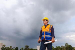 Ingenieur Mann mit Entwurf Überprüfung Projekt beim Infrastruktur Grundstück, Vorarbeiter Arbeiter im schwer Hüte auf Konstruktion Seite? ˅ foto