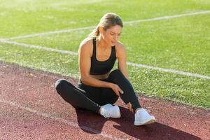 ein sportlich Frau sitzt auf ein Spur Feld im Schmerz, umklammern ihr Bein, vielleicht Leiden von Muskel Krampf oder Verletzung. foto