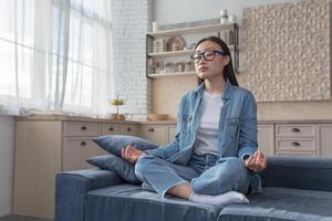 jung schön asiatisch Mädchen meditiert beim Zuhause Sitzung auf das Couch, ruhen während das Tag foto