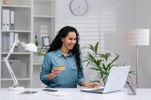 konzentriert spanisch Geschäftsfrau mit Laptop und Anerkennung Karte im ein modern Zuhause Büro Einstellung, vorbildlich Fernbedienung Arbeit und E-Commerce. foto