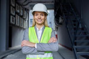 Porträt von reifen erfolgreich weiblich Ingenieur, Arbeiter im schwer Hut und reflektierend Weste mit gekreuzt Waffen lächelnd und suchen beim Kamera. foto