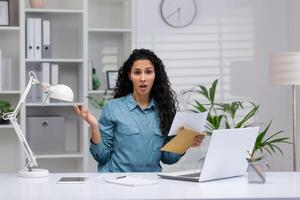 spanisch Geschäftsfrau beim Zuhause Büro suchen überrascht und besorgt während lesen Unterlagen, Darstellen Schlecht Nachrichten oder unerwartet Arbeit Komplikationen. foto