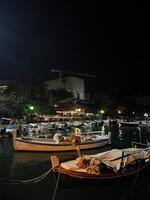 budva, Montenegro - - 25 Dezember 2022. Angeln Boote festgemacht aus das beleuchtet Küste von das Resort Stadt, Dorf beim Nacht foto