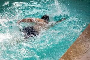 glücklich indisch Junge Schwimmen im ein Schwimmbad, Kind tragen Schwimmen Kostüm entlang mit Luft Tube während heiß Sommer- Urlaube, Kinder Junge im groß Schwimmen Schwimmbad. foto