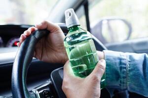 asiatische fahrerin hält kaltes wasser zum trinken im auto, gefährlich und riskiert einen unfall. foto