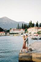 Mann und Frau Stand umarmen und fast küssen auf das Seebrücke von das uralt Dorf von Rose. lustica, Montenegro foto