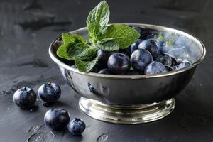 Blaubeeren im ein Silber Schüssel mit Minze Blätter, elegant, einfach Komposition foto