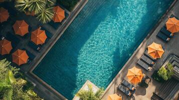 Antenne Aussicht von ein luxuriös Hotel Schwimmen Schwimmbad mit funkelnd Wasser, umgeben durch Orange Regenschirme und Sonne Liegen, Ideal zum Reise und Sommer- Urlaub Themen foto