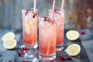 erfrischend Rosa Limonade im hoch Brille mit Eis, Strohhalme, und Zitrone Garnierung auf ein rustikal hölzern Tisch, perfekt zum Sommer- Parteien oder heiß Tage foto