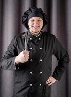 männlicher Koch, der Küchengeräte isoliert auf dunklem Vorhanghintergrund hält foto