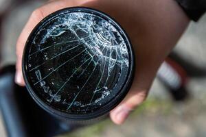 Hände von jung Fotograf halten dslr Foto Kamera mit gebrochen Linse Filter Glas nach wenn fallen Nieder auf zu das Boden. schließen hoch. zerstört geknackt Foto Filter. Makro. oben Sicht. selektiv Fokus.