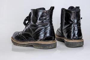 frontal Aussicht von ein sehr getragen Paar von Stiefel. alt benutzt gebrochen schwarz Leder Spitze hoch Stiefel. modisch Knöchel Stiefel. stilvoll Damen Herren unisex Grunge Stiefel mit Schnürsenkel. isoliert auf Weiß Hintergrund foto