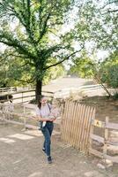 Mutter mit ein wenig Mädchen im ihr Waffen Spaziergänge Vergangenheit das hölzern Zaun von ein Koppel mit ein Pony im das Park foto