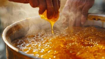 ein Hand Rühren ein groß Topf von frisch geerntet Honig mit Dampf steigend von es ist klebrig Oberfläche foto