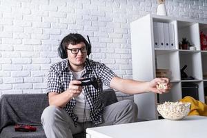 junger Mann, der zu Hause Videospiele spielt und Popcorn isst foto
