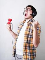 lustiger junger Mann, der schreit und Videospiele spielt, die einen Joystick auf grauem Hintergrund hält