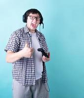 lustiger junger Mann, der Videospiele spielt und einen Joystick hält, der Daumen nach oben zeigt, isoliert auf blauem Hintergrund foto