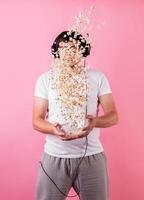 junger lustiger Mann, der Popcorn in die Luft wirft, isoliert auf Pink foto