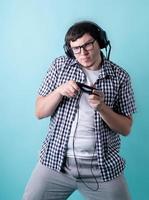 lustiger junger Mann, der Videospiele spielt und einen Joystick auf blauem Hintergrund hält foto