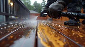 ein Paar von Hände mit ein Leistung Sprühgerät zu gleichmäßig Mantel ein hölzern Deck mit ein Reich Mahagoni beflecken bringen Neu Leben zu ein müde draussen Raum foto