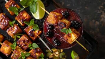 ein mojitoinspiriert Cocktail mit durcheinander Brombeeren Limette und Minze serviert neben ein Teller von knusprig Tofu Spieße mit ein Erdnuss Eintauchen Soße foto