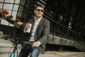 junger Geschäftsmann auf dem E-Bike mit Kaffeetasse zum Mitnehmen foto