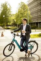 junger Geschäftsmann auf dem E-Bike mit Kaffeetasse zum Mitnehmen foto