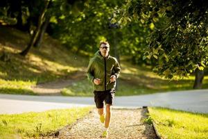 athletischer junger Mann, der beim Training im sonnigen grünen Park läuft