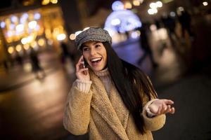 hübsche junge frau, die ihr handy zur weihnachtszeit auf der straße benutzt foto