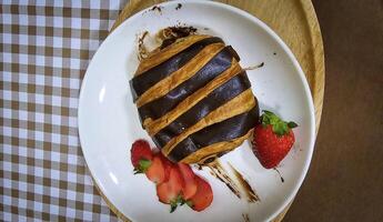 frisch hausgemacht gestreift Schokolade Croissant mit Schokolade Füllung auf ein runden Weiß Platte, serviert mit frisch Erdbeere foto