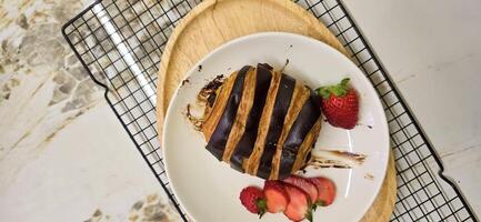 frisch hausgemacht gestreift Schokolade Croissant mit Schokolade Füllung auf ein runden Weiß Platte, serviert mit frisch Erdbeere foto