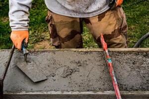 Maurer Verbreitung Beton mit ein Kelle und Niveau zu bauen ein Mauer beim ein Konstruktion Seite? ˅ foto