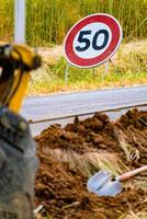 Arm von ein Mini Gräber und Eimer mit ein Geschwindigkeit Grenze Zeichen beim 50, Straße Zeichen foto