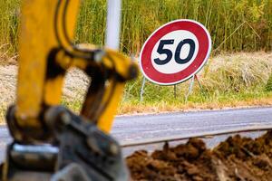 Arm von ein Mini Gräber und Eimer mit ein Geschwindigkeit Grenze Zeichen beim 50, Straße Zeichen foto