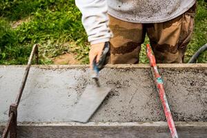 Maurer Verbreitung Beton mit ein Kelle und Niveau zu bauen ein Mauer beim ein Konstruktion Seite? ˅ foto