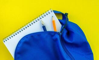 Schule Rucksack, Bleistift, Stift und Notizblock auf ein Gelb Hintergrund. foto