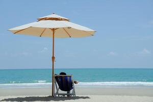 Menschen Sitzung auf Salon Stühle auf tropisch Strand unter Regenschirme, Weiß Sand, Meer, kühlen, entspannen, Ferien foto