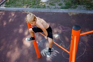 ein Sport Junge kletterte oben das horizontal Bar zu ausführen ein Sport Element. Straße trainieren auf ein horizontal Bar im das Schule Park. foto