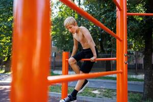 ein Fitness Kind kletterte zwischen das Fitnessstudio Riegel. Straße trainieren auf ein horizontal Bar im das Schule Park. foto