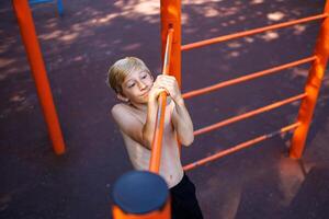 das Fitness Teenager gepackt das Bar mit beide Hände und gezogen zurück. Straße trainieren auf ein horizontal Bar im das Schule Park. foto