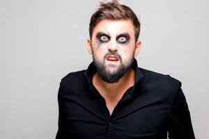 ein Mann mit ein Bart und bilden im das Stil von das Untote auf Halloween geöffnet seine Mund und zeigt an seine Zähne foto